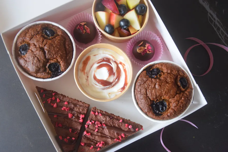 Brunch Natuurlijk is een box met natuurlijke lekkernijen zoals brownie, vanillemuffin met blauwe bes, dadelbonbon met rozenblaadjes, een bakje Rauw Power Hangop met frambozenspread en een verse fruitsalade